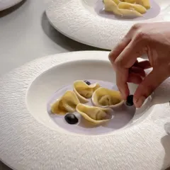 A chef carefully plating tortellini in a lavender-colored sauce. This dish was part of a menu where each course was designed to reflect the balance and form of the art at Galerie Isa.