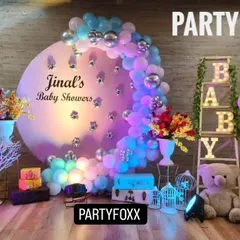 An elegant baby shower setup for Jinal, featuring a large circular backdrop with a crescent of blue and pink balloons, light-up "BABY" letters, and floral arrangements.