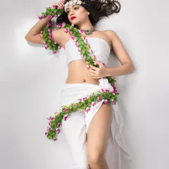 This is from a conceptual shoot inspired by Gaia, the goddess of nature. The model lies on a white background, draped in white fabric and a garland of flowers, creating a mythical and ethereal portrait.
