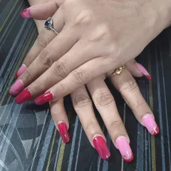 A client showing off her new set of custom press-on nails. This design features a mix of pink and red with a delicate silver line accent for a stylish, mismatched look.