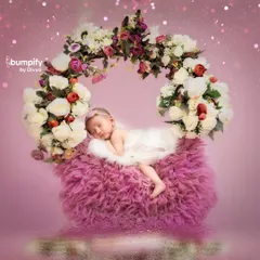 A dreamy and magical portrait of a newborn sleeping on a floral swing. The combination of soft pink fur and a lush flower wreath creates a fairytale-like image.