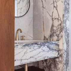 A glimpse into a powder room in Apartment 5026, where we used dramatically veined marble to create a bold statement. The classic brass faucet and simple round mirror complement the stone, creating a look that is both vintage and timeless.