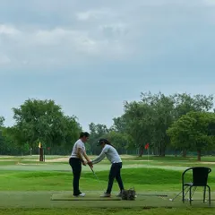 A coach provides hands-on instruction to a new golfer, adjusting her grip and setup. This personalized attention is key to building a solid foundation in the game.
