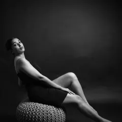 This full-body monochrome portrait plays with negative space and form. The simple pose and dark background create a minimalist and elegant composition, perfect for a model's portfolio.