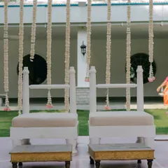 Elegant white chairs for the bride and groom, set against a backdrop of hanging tuberose garlands for a clean and classic look.