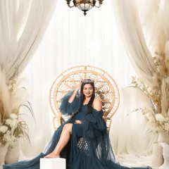 A confident and glamorous studio shot of a mom-to-be in a teal gown, seated on a peacock chair. The dramatic lighting and pose give this portrait a high-fashion feel.
