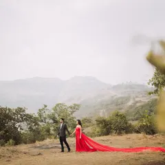 A breathtaking wide-angle shot in the hills of Lonavla. The bride's long, flowing red gown creates a stunning trail against the natural landscape, making for a truly epic pre-wedding photo.