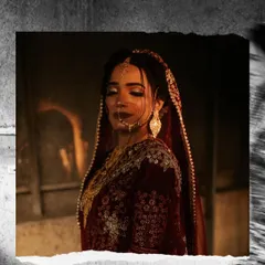 A beautiful bridal portrait with a moody, cinematic feel. The warm light highlights the intricate details of her deep red lehenga and jewelry.