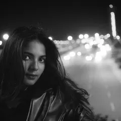 A striking black and white night portrait of a woman looking directly at the camera, with the blurred lights of a highway stretching out behind her. This shot exemplifies my raw, urban cinematic style.