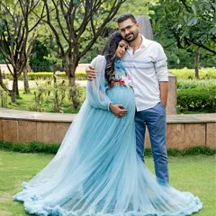 A fairytale moment in the park. The mom-to-be looks stunning in a flowing light blue gown, sharing a tender embrace with her partner.