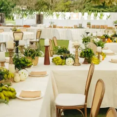 The tables at our 'Easy Breezy Brunch' are adorned with centerpieces of fresh bananas, grapes, and apples, mixed with simple white flowers. The decor embraces a monochromatic palette of ivory, beige, and green for a calm, natural feel.