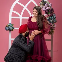 A beautiful studio maternity portrait where the husband-to-be kneels to kiss his wife's baby bump. The scene is set against a decorative arch with flowers, adding a touch of elegance.