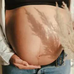 A creative close-up focusing on the baby bump. The shadow of a pampas grass frond adds an interesting texture and artistic element to the shot.