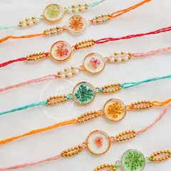 A close-up of the round floral rakhis, each with unique dried flowers and delicate pearl and gold beadwork.