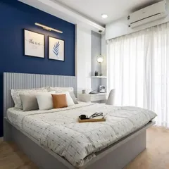 This master bedroom features a bold navy blue accent wall behind a fluted panel headboard. A compact, wall-mounted desk next to the bed serves as a convenient workspace.