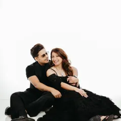 A relaxed and intimate portrait of a couple sitting on the floor against a clean white backdrop. This minimalist studio setup allows their connection and stylish black attire to be the main focus, creating a timeless and elegant pre-wedding photograph.