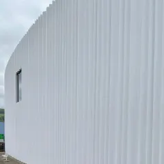 The corrugated white facade of a building at the Vitra Campus by SANAA. The simplicity of the form is animated by the rhythmic play of light and shadow across its surface.