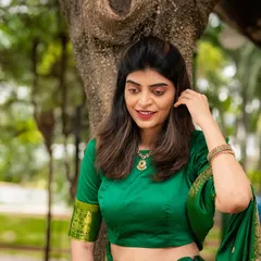 A graceful outdoor portrait of a woman in a green saree. The natural setting complements the traditional attire perfectly.