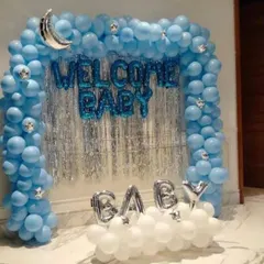 A classic "Welcome Baby" setup perfect for a home celebration. This design uses a blue balloon arch over a silver fringe curtain, with foil letters and a cloud of white balloons at the base.