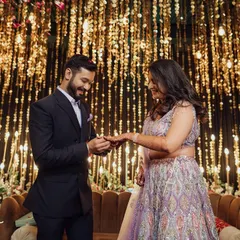 The ring exchange. A classic, happy moment from an engagement ceremony, captured against a glittering backdrop of fairy lights.