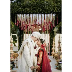 A tender moment under the mandap. The couple shares a quiet, intimate forehead kiss, framed by the beautiful floral decorations of their wedding ceremony.