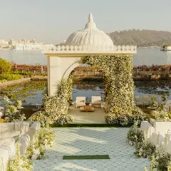 A serene, all-white mandap seemingly floating on the water at Jagmandir, Udaipur. This minimalist yet breathtaking design, framed by an arch of white flowers, highlights the natural beauty of the destination.