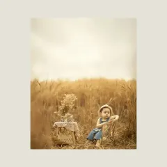 A wide shot showing the child and the picnic setup in the middle of the golden field. This image captures the scale and beauty of the natural surroundings, creating a dreamy and picturesque scene.