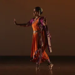 A faculty member performs a graceful Bharatanatyam piece at SparkLights 2024. The traditional orange and purple costume and expressive posture are beautifully captured under the warm stage lights.