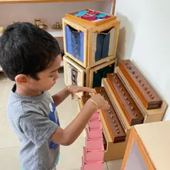 A child works with the Pink Tower, a classic sensorial material. This activity helps them visually discriminate between sizes and builds their understanding of dimensions, which is an indirect preparation for mathematics.