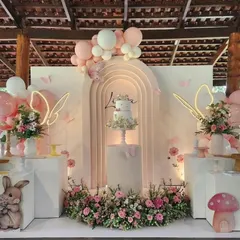 This outdoor butterfly-themed birthday features a stunning white arched backdrop with neon butterfly lights and lush floral arrangements. The setup is perfect for a dreamy garden party aesthetic.