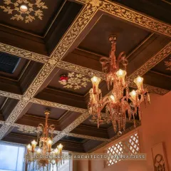The ceiling is a fifth wall that deserves just as much attention. Here, we designed a dark wood coffered ceiling with intricate gold-painted floral patterns and hung opulent crystal chandeliers to create a truly grand and royal ambience.