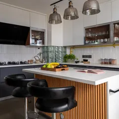 A stylish and functional kitchen with transitional charm and industrial flair. The island with a fluted wood base and comfortable bar stools serves as a casual dining spot, illuminated by glass pendant lights.