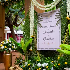 A welcome sign for a traditional wedding ceremony with a 'Banana Grove' theme. The decor features woven banana leaves, fresh flowers, and tender coconuts for a natural and authentic feel.