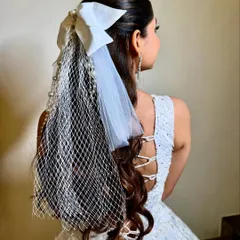 A unique and modern reception hairstyle featuring a half-updo with a large white bow and an attached pearl-studded net veil. This is a fashion-forward choice for the contemporary bride.
