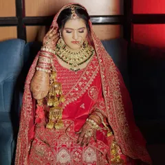 A regal bridal portrait. The bride is wearing a magnificent red velvet lehenga with heavy jewelry, and the makeup is designed to be equally grand, with bold eyes and a perfectly sculpted face.