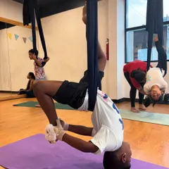An instructor helps a young student with an inverted aerial pose. Safety is our top priority, and we provide hands-on guidance to ensure every child feels secure.
