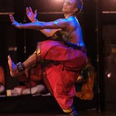 A dynamic shot from a solo performance, capturing a moment of powerful movement and expression. The red costume and blue light create a striking contrast.
