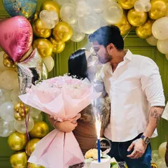 A romantic moment captured during an anniversary celebration. The warm glow of the neon sign and the festive balloons create a beautiful atmosphere.