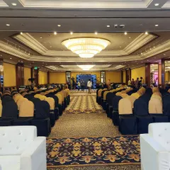 A wide shot of a large ballroom set up for a corporate conference. The seating is arranged theatre-style, facing a stage with a large screen, demonstrating our capability to handle large-scale corporate events.