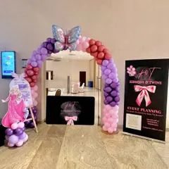 The party entrance, featuring a balloon arch in shades of purple and pink, topped with a large butterfly balloon. My company banner and a welcome sign greet the guests.