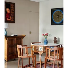 This cozy corner of the living area features a traditional Indian card table with inlaid tiles and chairs, set against a backdrop of unique art pieces collected by the family.