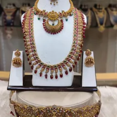 A beautiful antique-finish set with a crescent-shaped choker and a matching long haram, studded with red stones. The set includes a traditional vaddanam (waist belt).