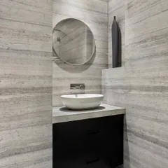 This bathroom, though lacking natural light, feels bright and spacious due to the use of horizontally grained stone walls and a large circular mirror. The minimalist design and clean lines create a serene and modern powder room.
