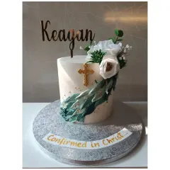 A modern and elegant confirmation cake. The design features a beautiful arrangement of white sugar flowers, succulents, and a gold cross.