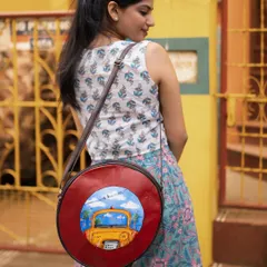 A fun and quirky hand-painted sling bag with a "Pili Taxi" design. The circular shape and colorful art make it a unique statement piece, paired here with a casual co-ord set.