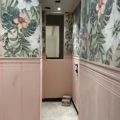 A work-in-progress view of a powder room, showing the installation of floral wallpaper above classic pink wainscoting. This demonstrates the layering of textures and patterns.