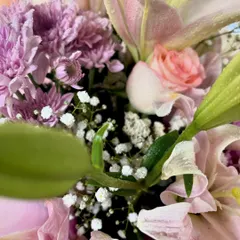 A different angle of the fresh flower arrangement, showing the green leaves and baby's breath that add fullness and contrast to the pink and purple blooms.