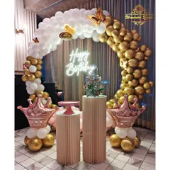 This elegant birthday decoration features a beautiful arch of white and chrome gold balloons, accented with butterfly details and rose gold crown balloons. The setup is completed with stylish plinths and a modern neon 'Happy Birthday' sign.