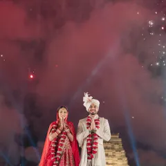A moment of gratitude and joy. The couple greets their guests after the varmala, surrounded by red smoke and a sky lit with fireworks, creating a powerful and colorful memory.