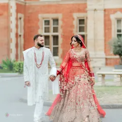 A romantic portrait of a couple during their London wedding, showcasing their intricate red and white traditional outfits against a classic British architectural backdrop.
